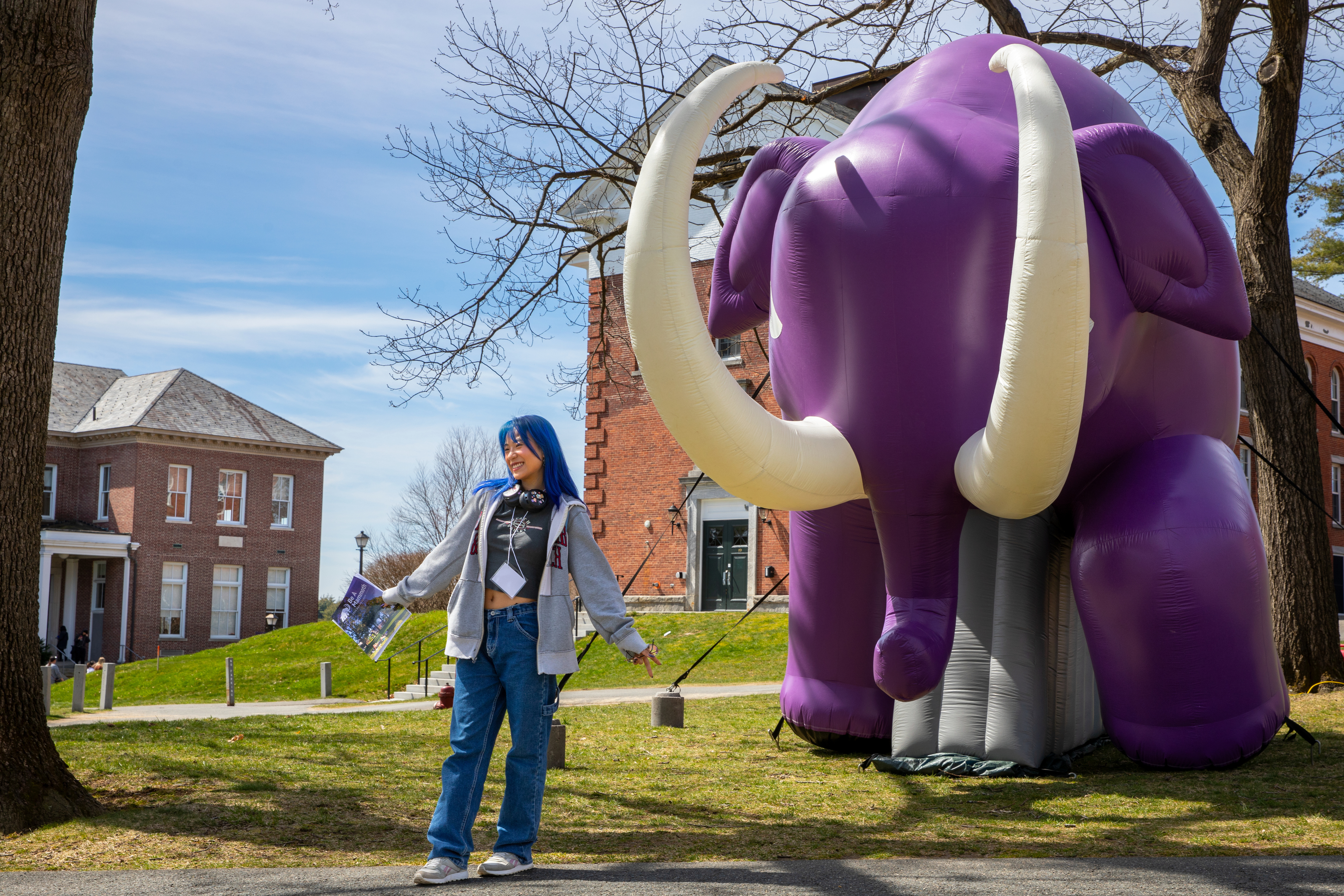 A woman poses in front of a large purple blow up mammoth.