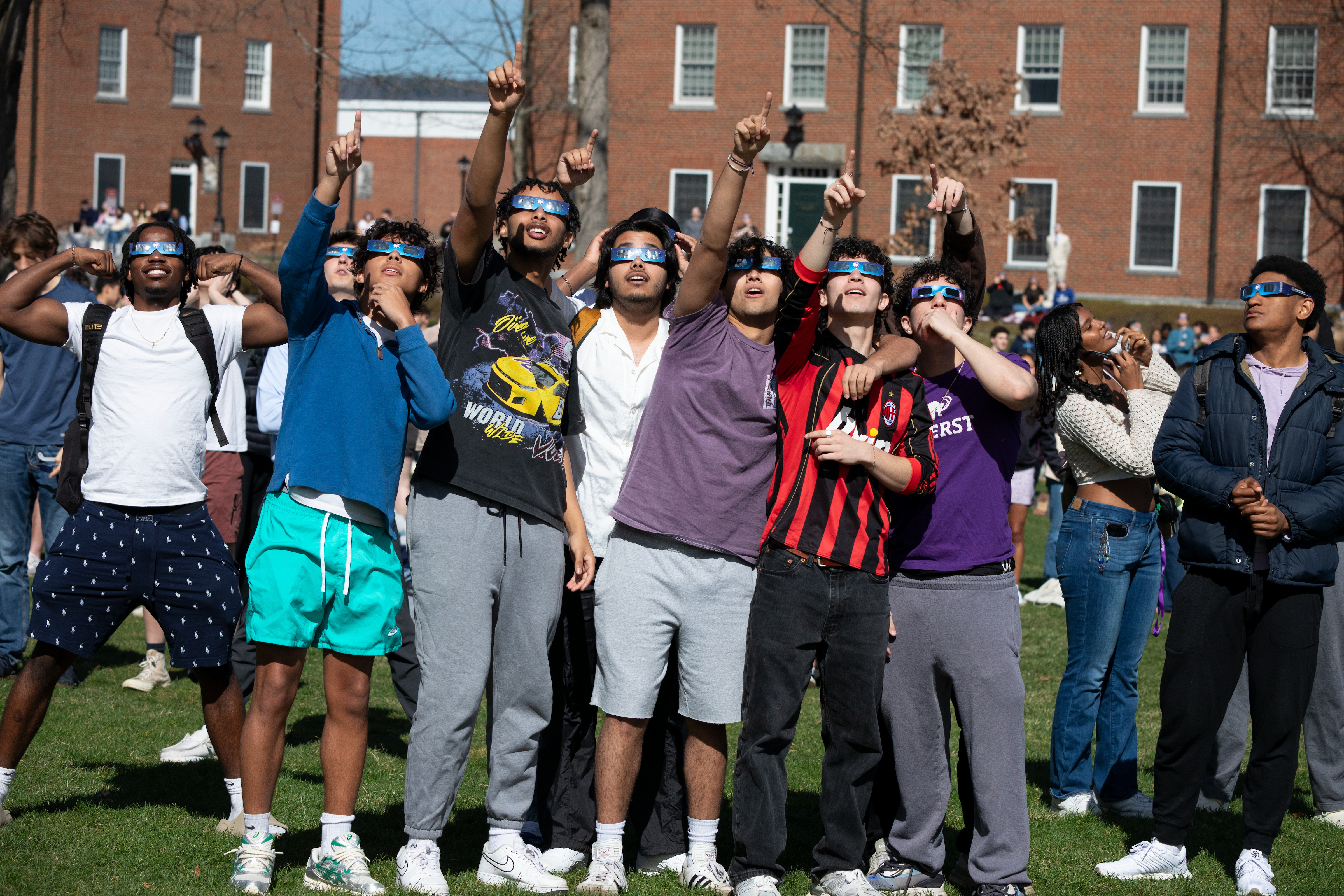 A group of people wearing eclipse glasses pointing at the sky.