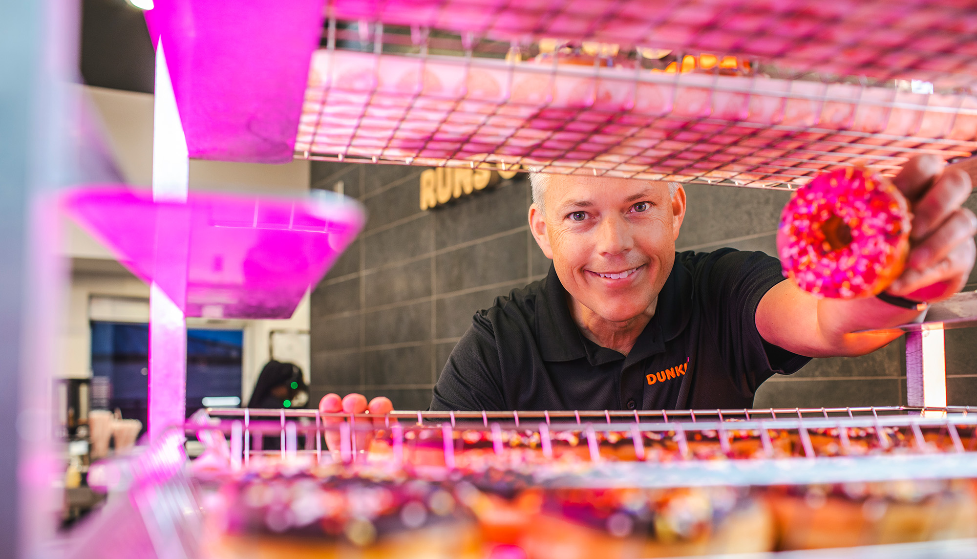 A man looking through a colorful, brightly lit case of donuts