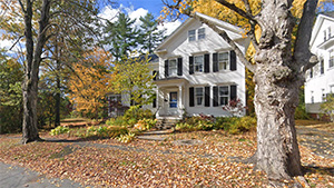 A two story white house surrounded by fall foliage
