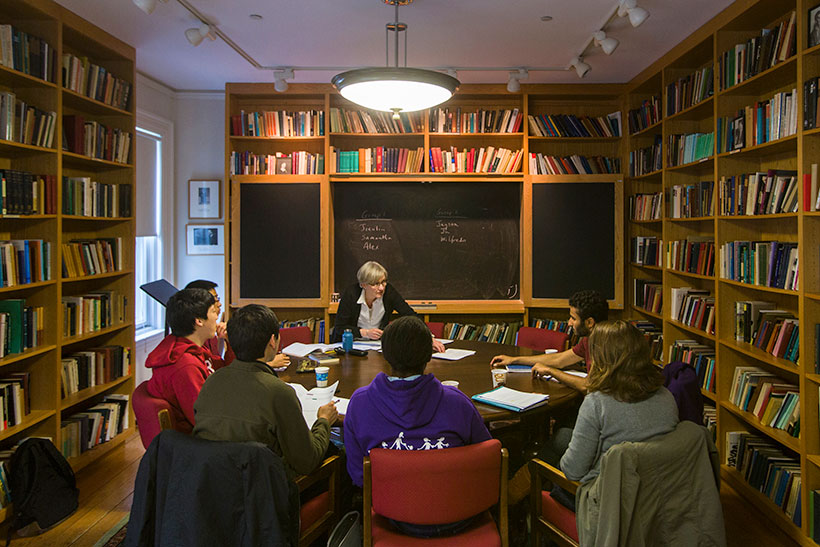 A professor teaches a small class in a booklined room