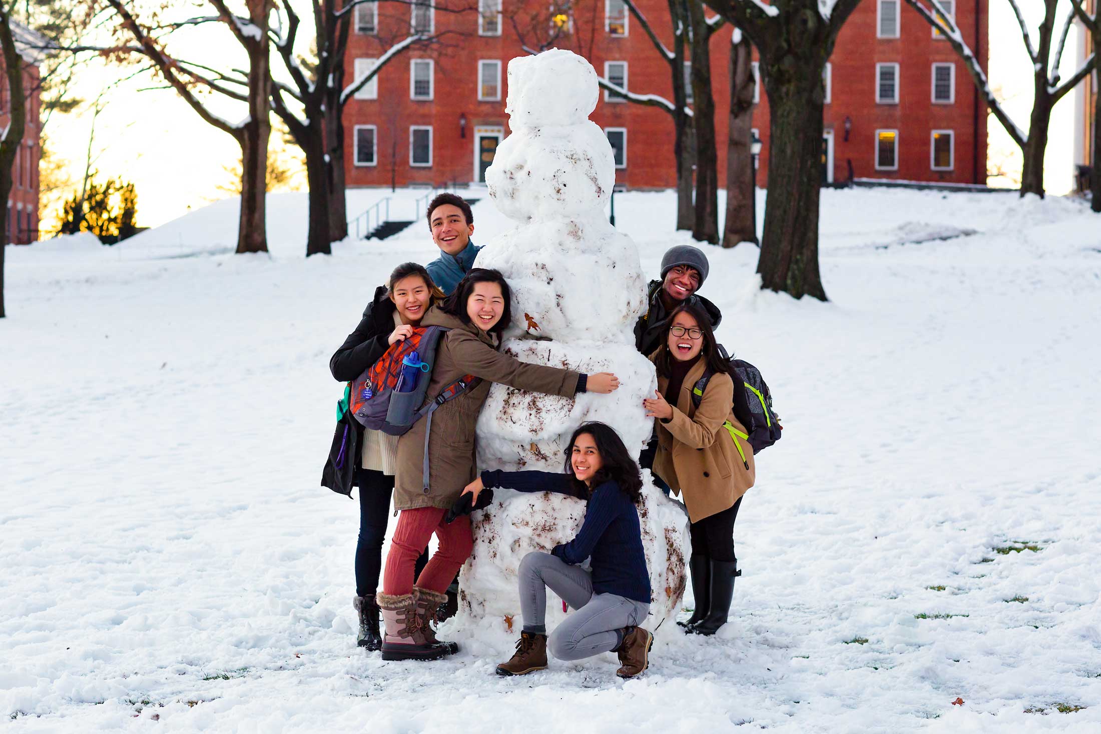 Six students gather around a large snowman