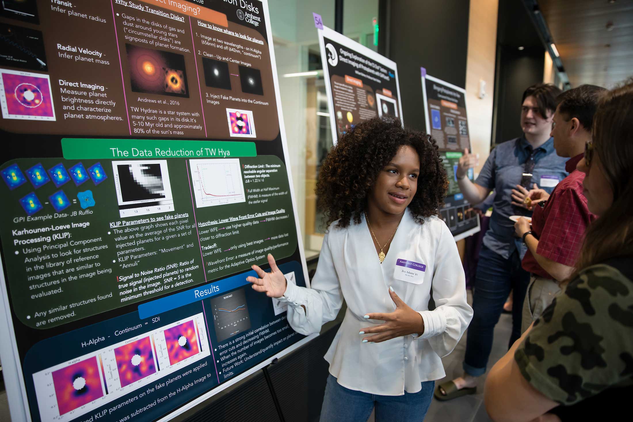 A student describes her summer research which is illustrated on a large poster