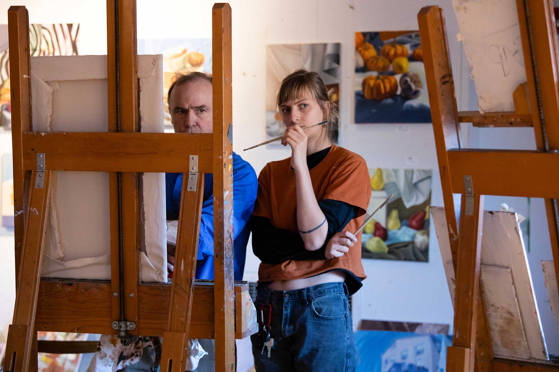 Two people stand before an easel contemplating a painting in progress