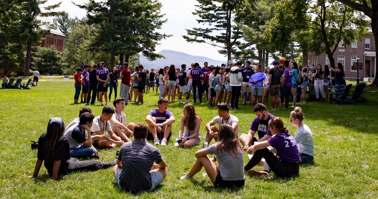 diverse group of students sitting on the grass on a sunny day on the quad with mountains in the distance