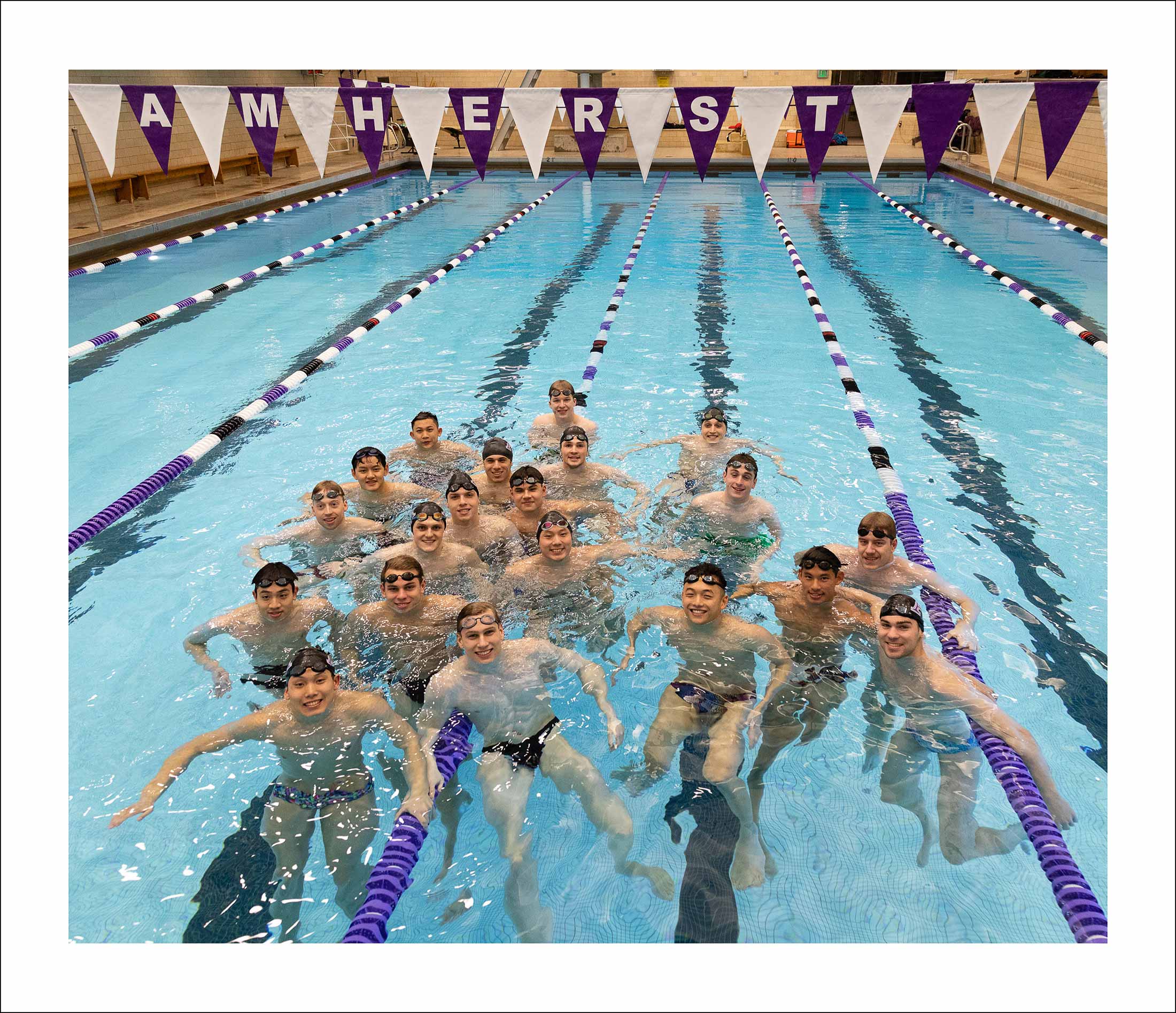 A large group of men smiling at the camera from inside of a swimming pool