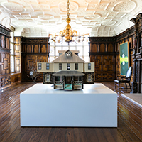 A room in a museum with a giant model house in the middle of the room