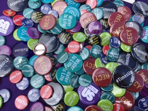 Multi-colored buttons are displayed in a cluster on top of one another, with phrases like "Water if Life" and "Times Up" on them, indicating favor of various social justice causes