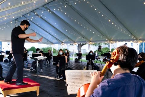 Mark Swanson leading the orchestra through practice in an outdoor tent.