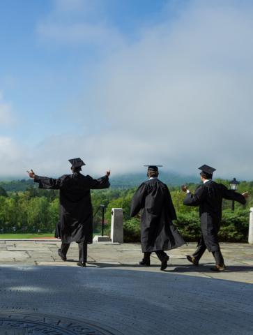 three graduates walk down the steps from Memorial Hill with blue sky ahead of them