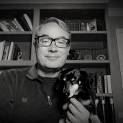 A black and white photo of an older man with glasses holding a dog